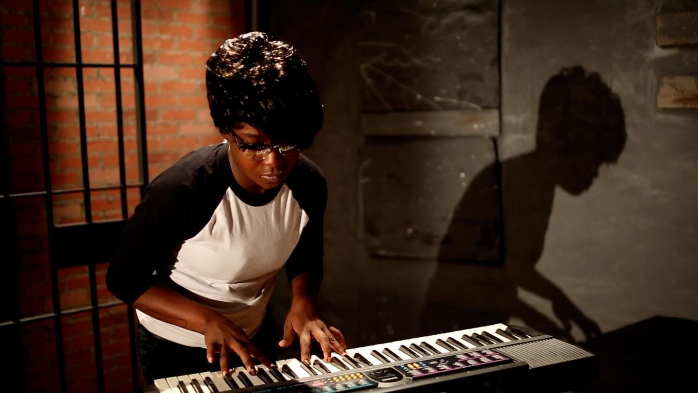 Person playing a keyboard in a dimly lit room, with warm light and a shadow cast on the wall.