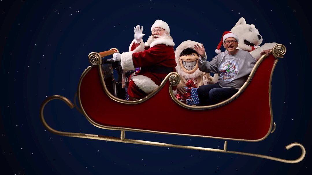 Three children in Santa outfits ride in a red sleigh on a dark blue background.