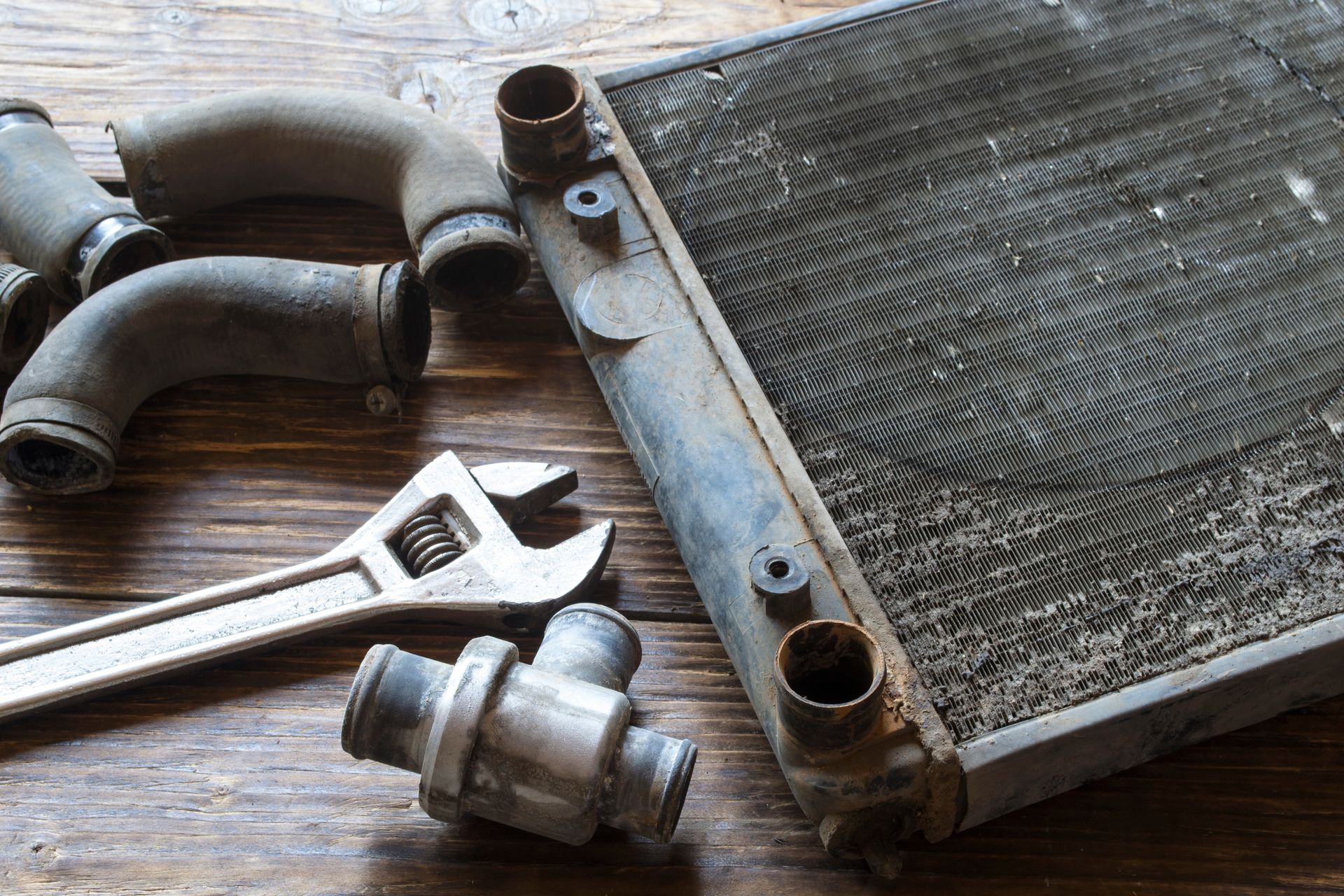 Car radiator with hoses and an adjustable wrench on a wooden work surface.