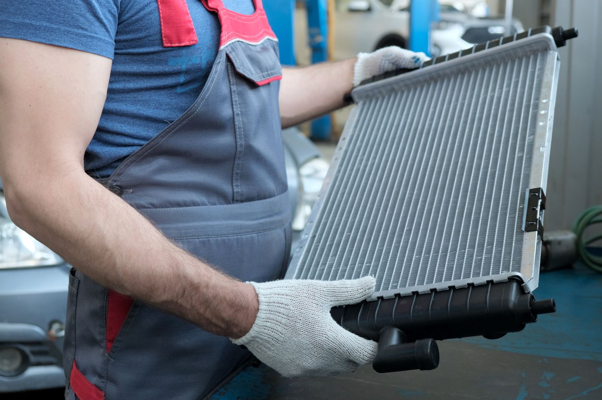 Technician holding a new automotive radiator during inspection inside a professional repair shop.