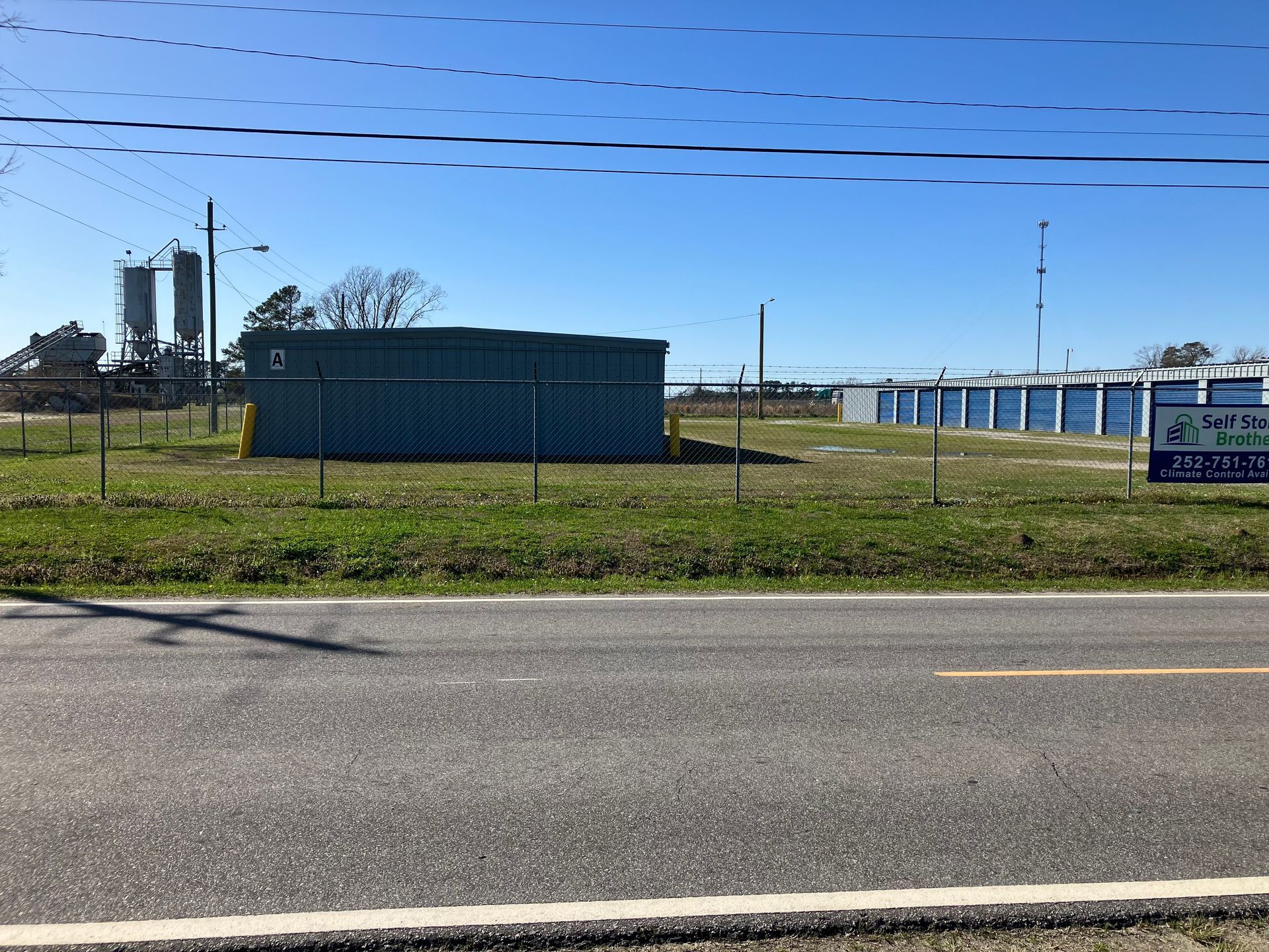 Blue self storage buildings behind a roadside fence under a clear sky