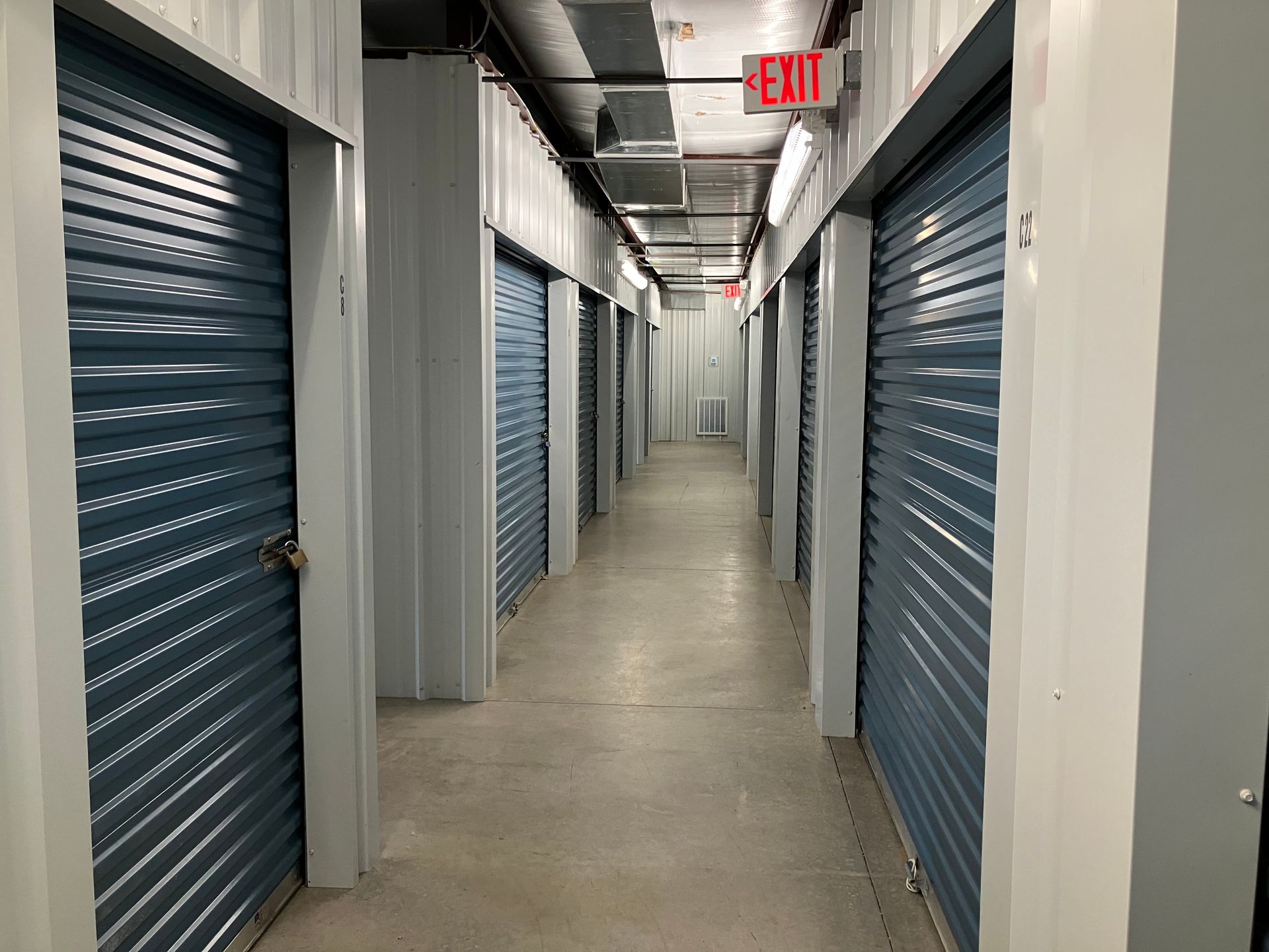 Long storage hallway with blue roll-up doors and an exit sign overhead