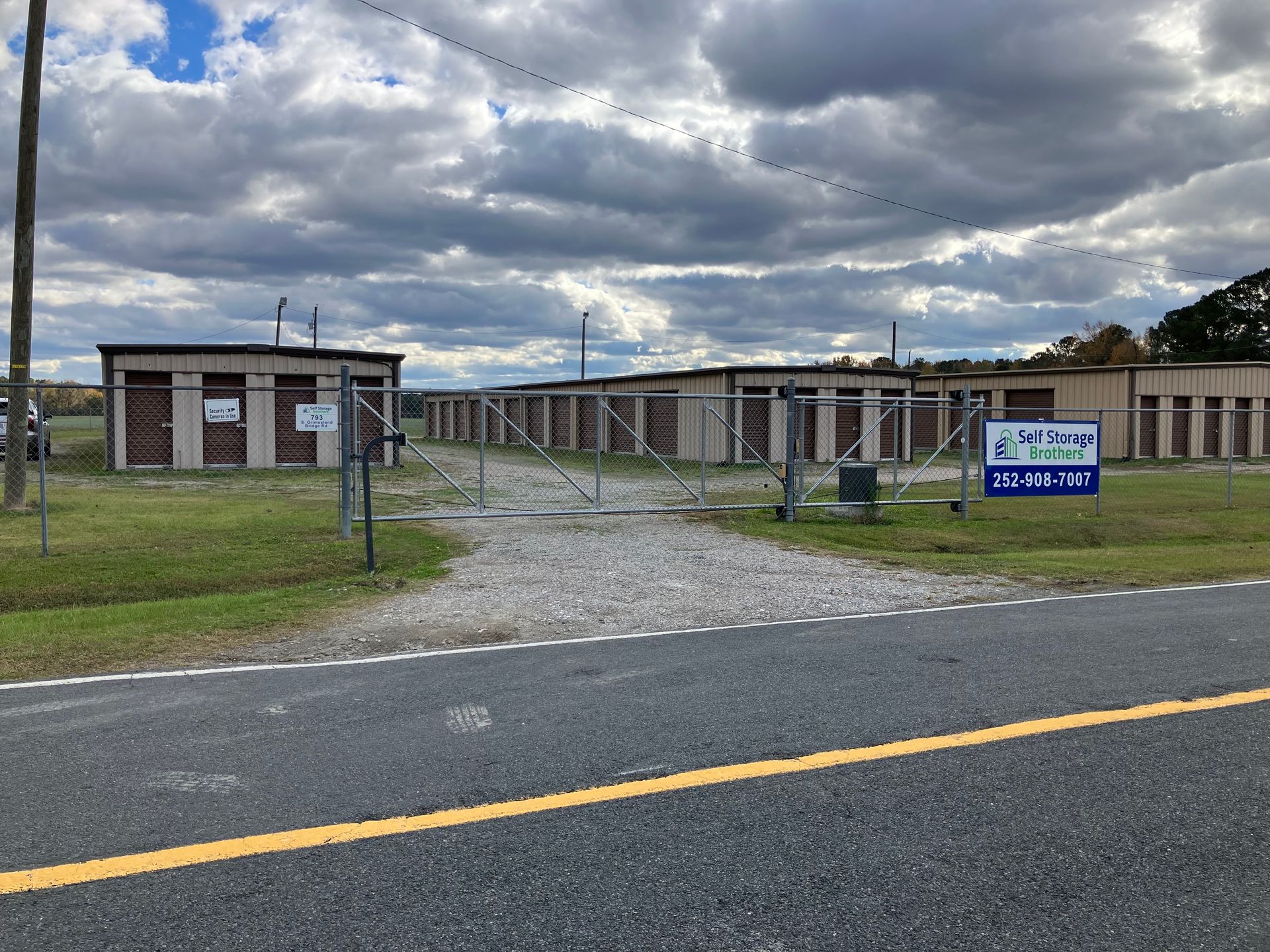 Rural roadside entrance to a low building behind a chain-link gate under cloudy skies