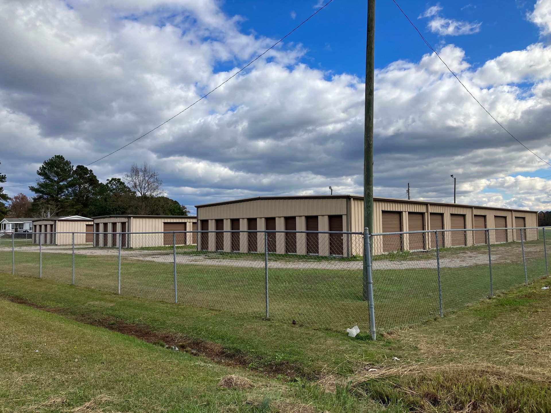 Chain-link fence around a beige utility building under a cloudy blue sky.