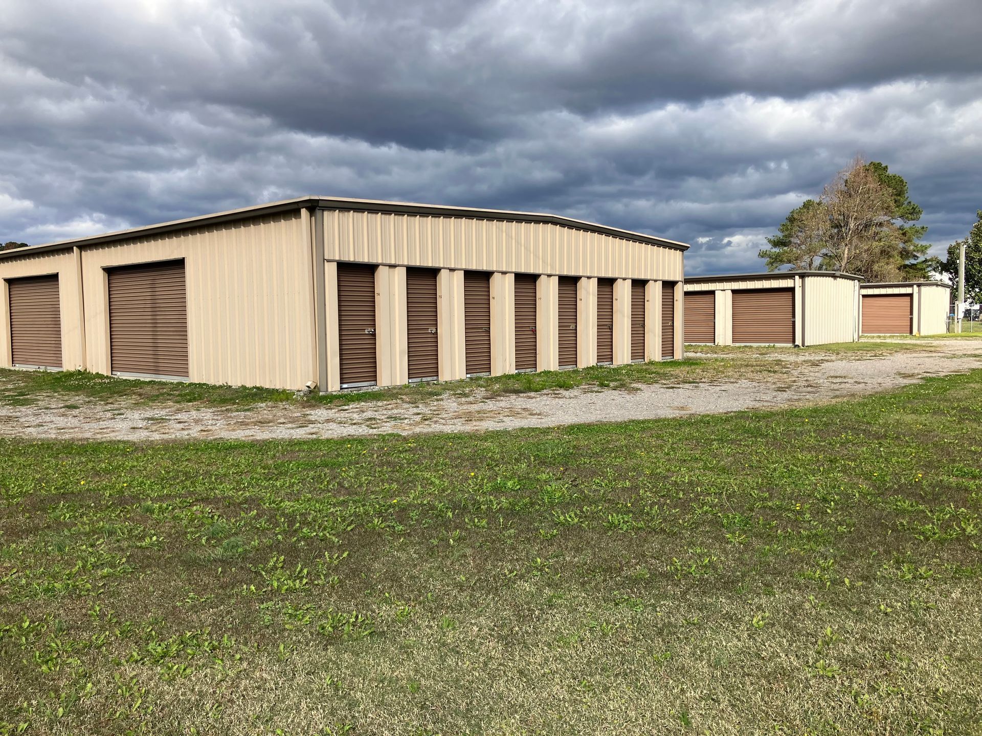 Tan metal self storage buildings on a grassy lot 