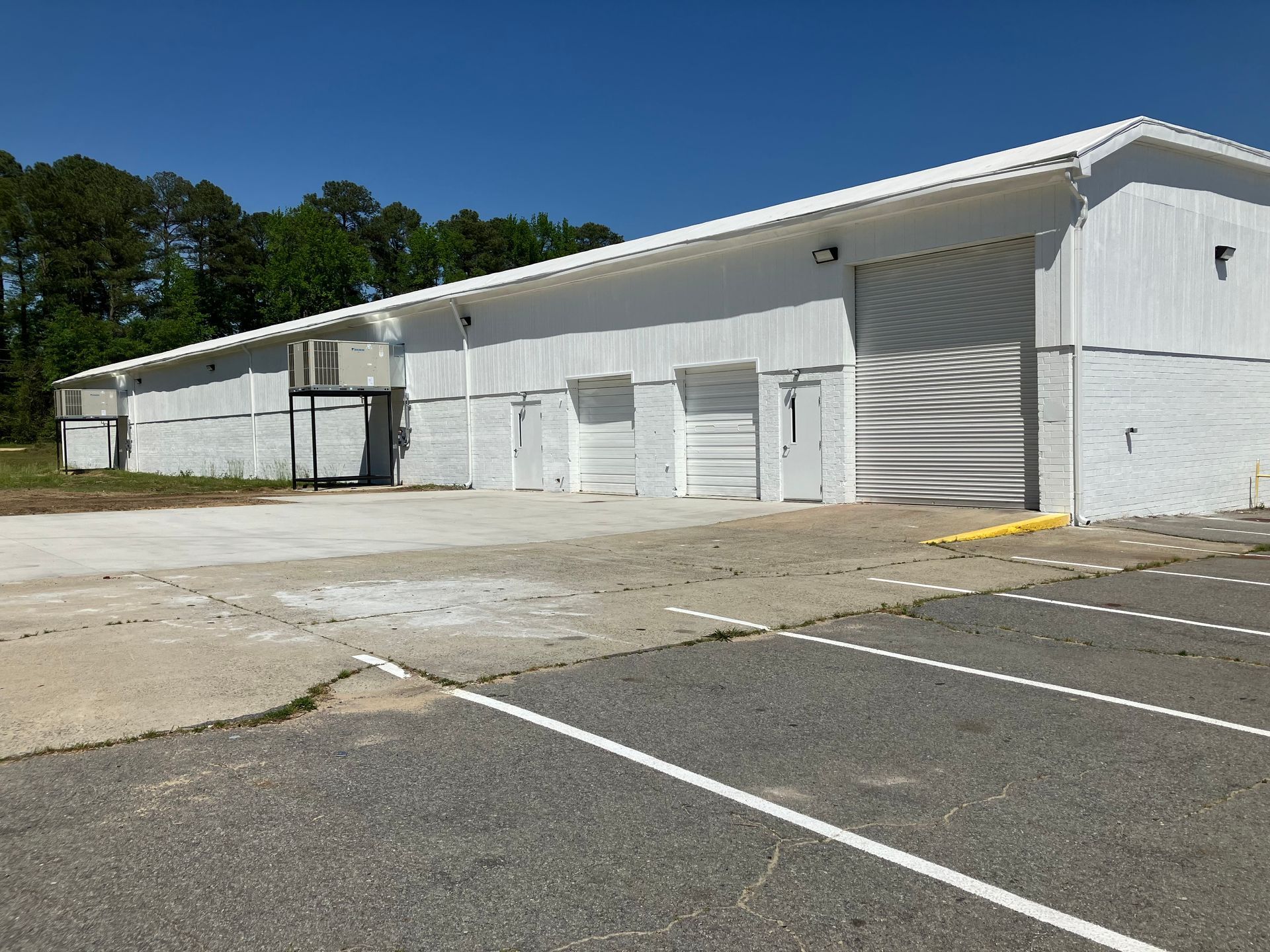 White industrial storage warehouse with loading dock doors and empty parking lot under a clear sky