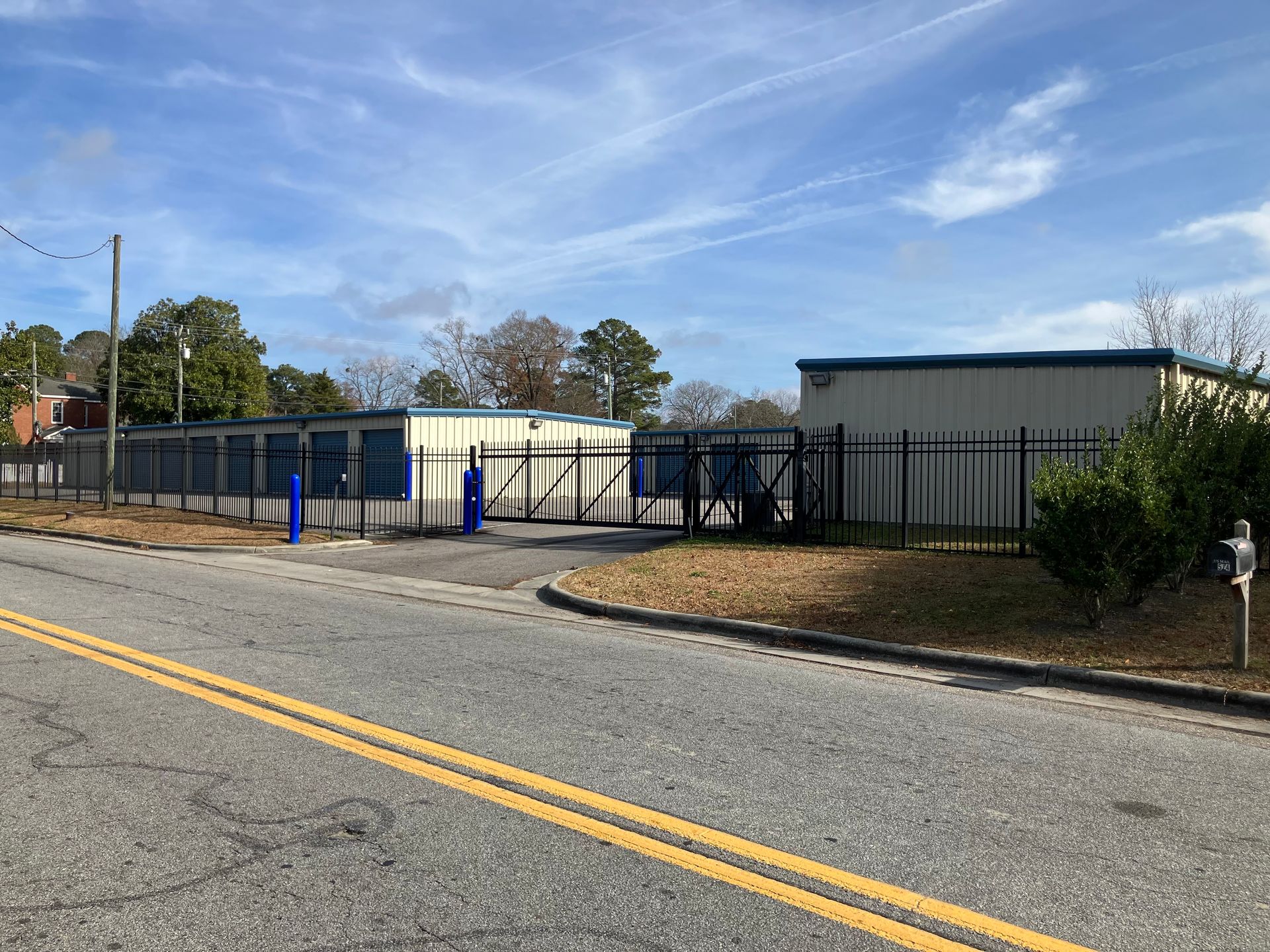 Blue fence and gate at a small industrial building beside a road under a clear sky