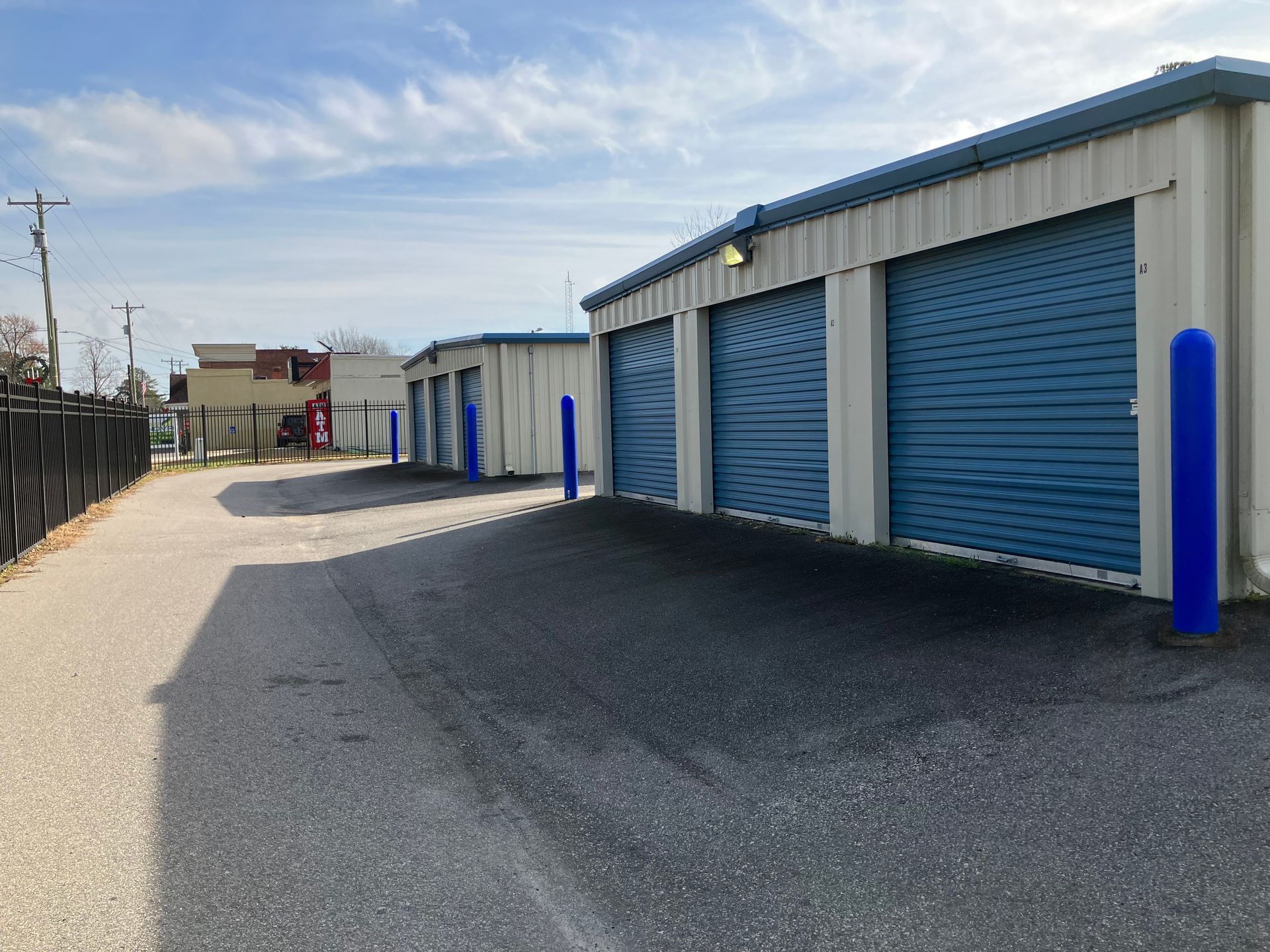 Row of blue roll-up storage unit doors along a gravel lane on a sunny day