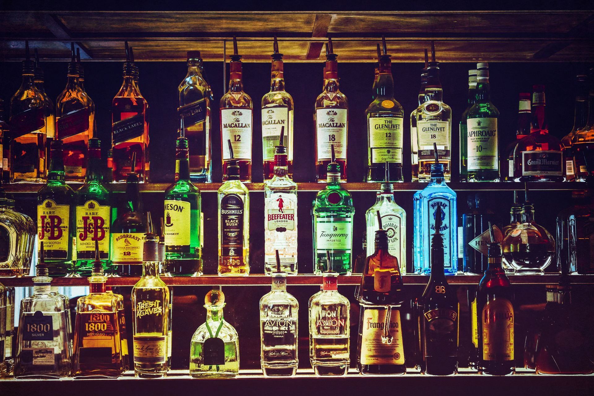 Bar shelves lined with various liquor bottles in different colors and sizes, dimly lit.