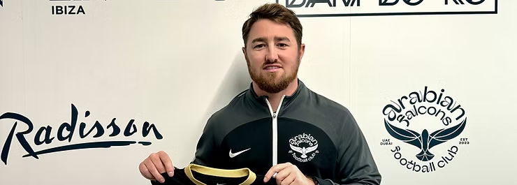 Man holding up a black football jersey at a sponsor backdrop with Radisson, Catalyst, and Flanels logos.