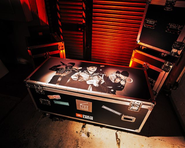 Black stage equipment case with band artwork under red lighting in an industrial backstage area