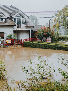 Flooded residential street beside a house with brown water covering the front yard and road