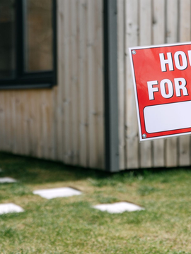 Red house-for-rent sign in front of a building and grassy yard