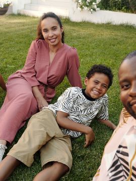 Four people sitting on grass outdoors, smiling at the camera in a sunny yard.