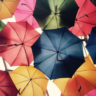 Colorful umbrellas overlapping overhead in pink, blue, yellow, red, and green hues