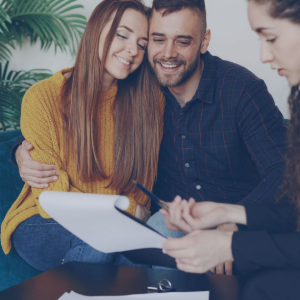Two smiling people review a clipboard with an advisor at a table indoors