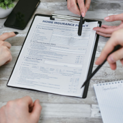 Hands reviewing a home insurance policy form on a clipboard with a pen on a table