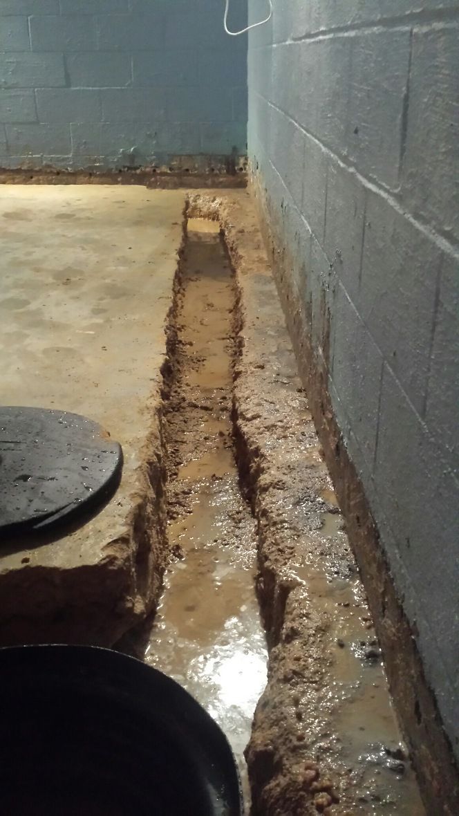 A drain in a basement next to a brick wall.
