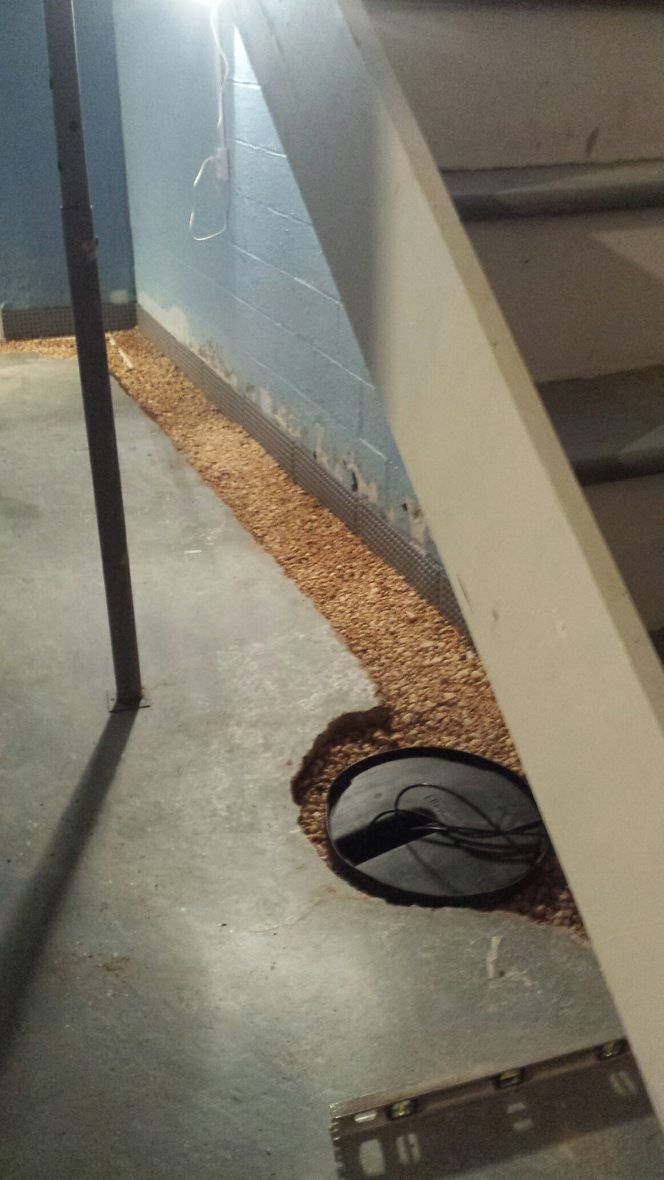 A drain hole in the floor of a basement next to a staircase.