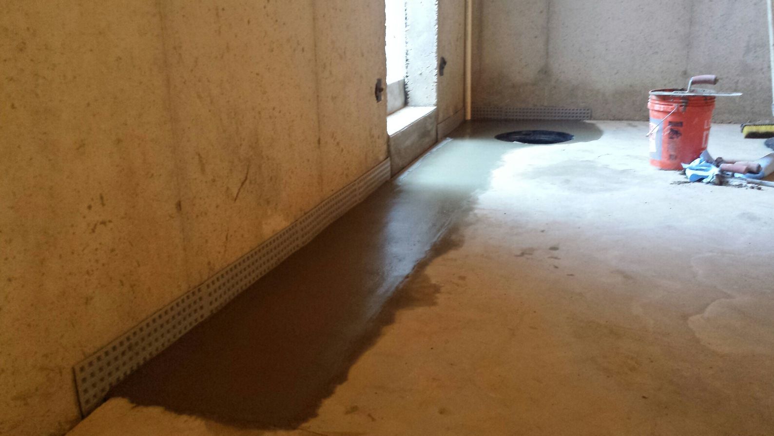 A concrete floor in a basement with a bucket on the floor.