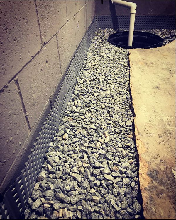 A pile of gravel next to a pipe in a basement