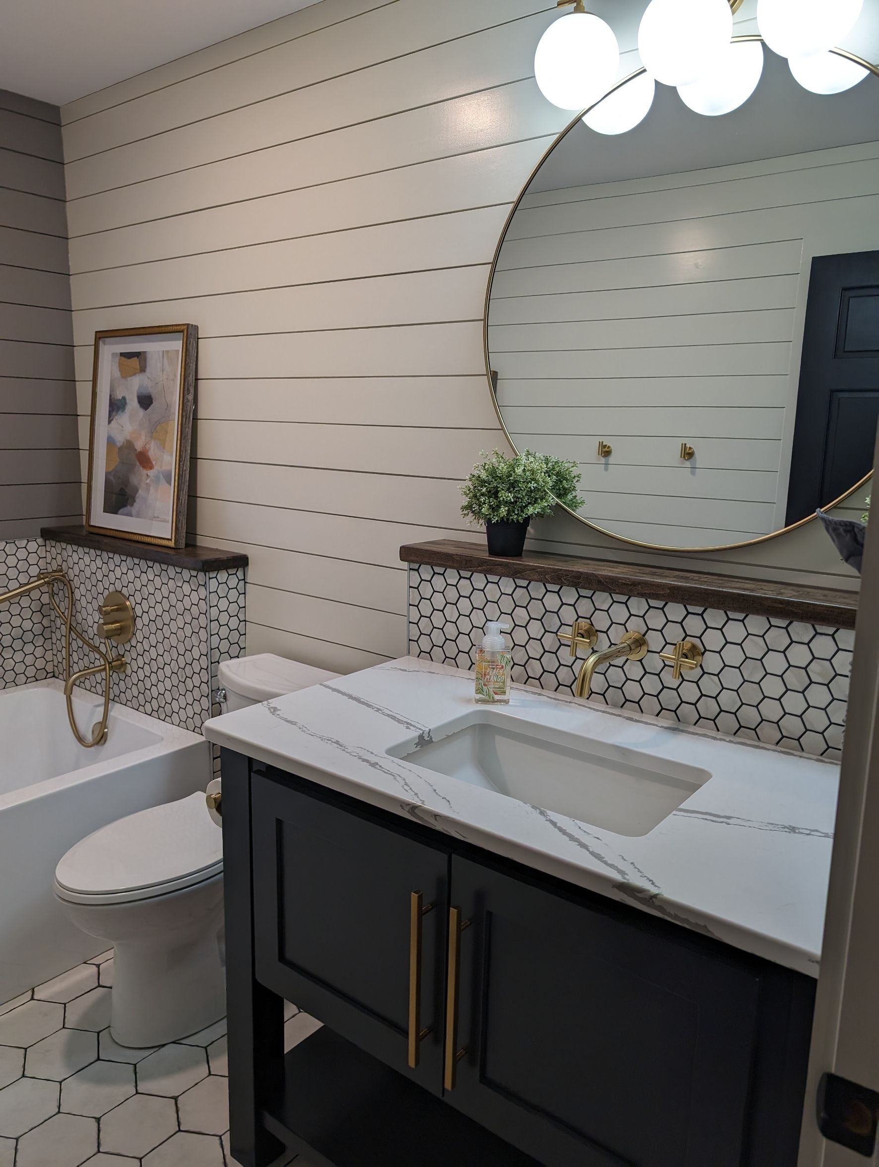 Modern bathroom with double vanity, round mirror, patterned tile, and a toilet beside a framed artwork