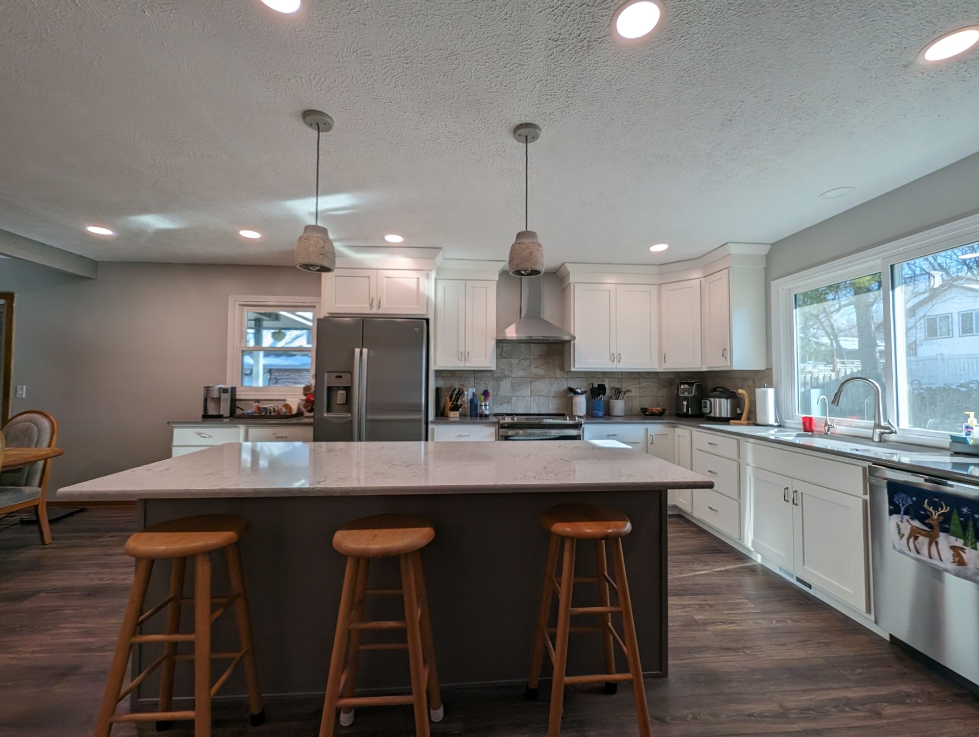 Bright modern kitchen with white cabinets, island, stools, and large window over sink