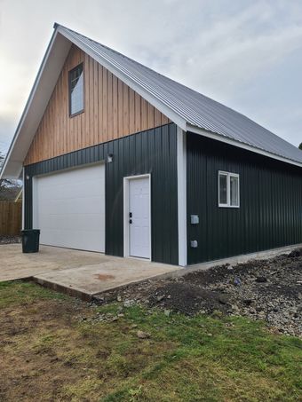 A house under construction with a new roof and porch, surrounded by gravel and trees.