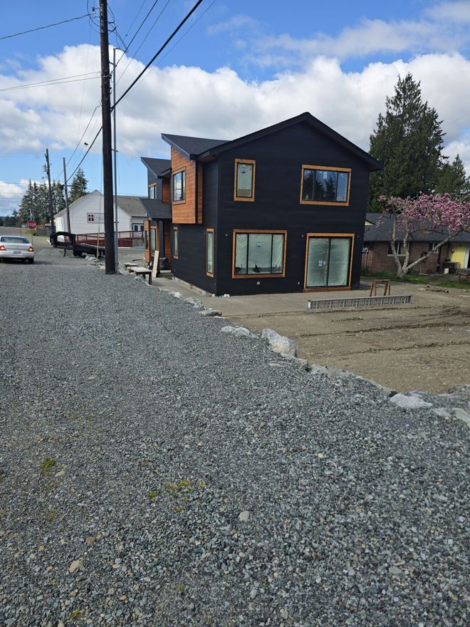 Black two-story modern house with brown trim and light gravel yard under a blue sky.