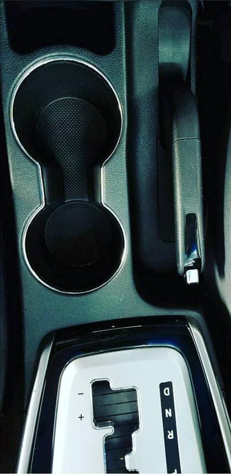 Car's center console with cupholders, gear shift, and parking brake. Black and silver tones.