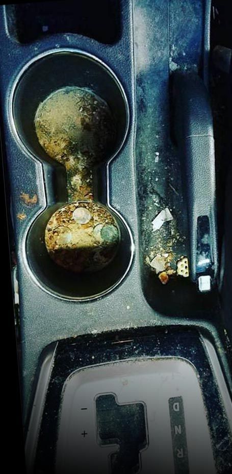A car's dirty console with two cup holders.  Debris and grime fill the holders and surrounding areas. The gearshift is visible.