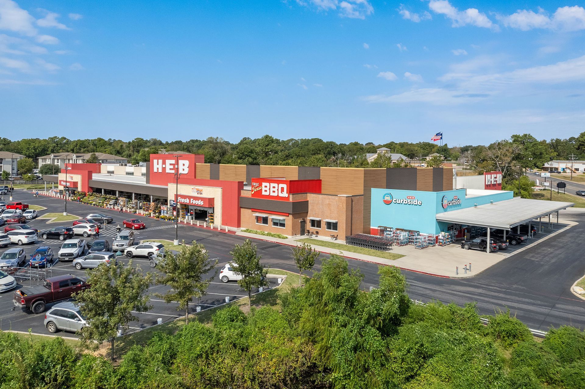 An aerial view of a HEB grocery store with a lot of cars parked in front of it near The Heights offers student apartments for rent near SHSU in Huntsville, TX.