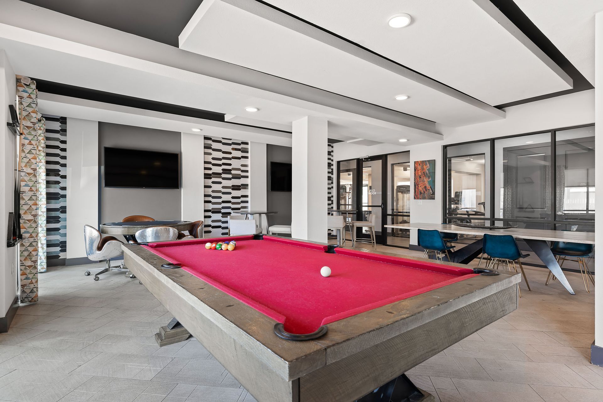 Red color pool table in the middle of the game room surrounded by seating areas with a TV at The Heights offers student apartments for rent near SHSU in Huntsville, TX.