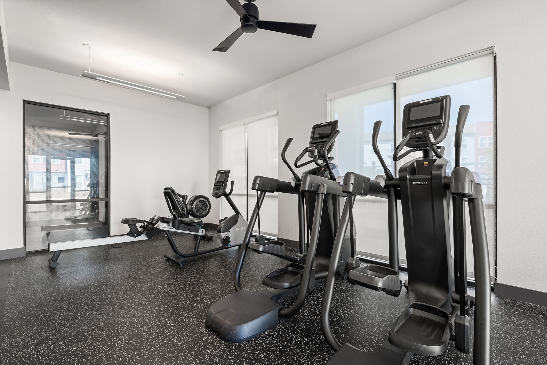 A gym with a lot of exercise equipment and a ceiling fan at The Heights offers student living in Huntsville, TX.