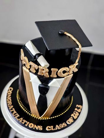 Graduation cake decorated with a black mortarboard, gold lettering, and a tuxedo design, reading 