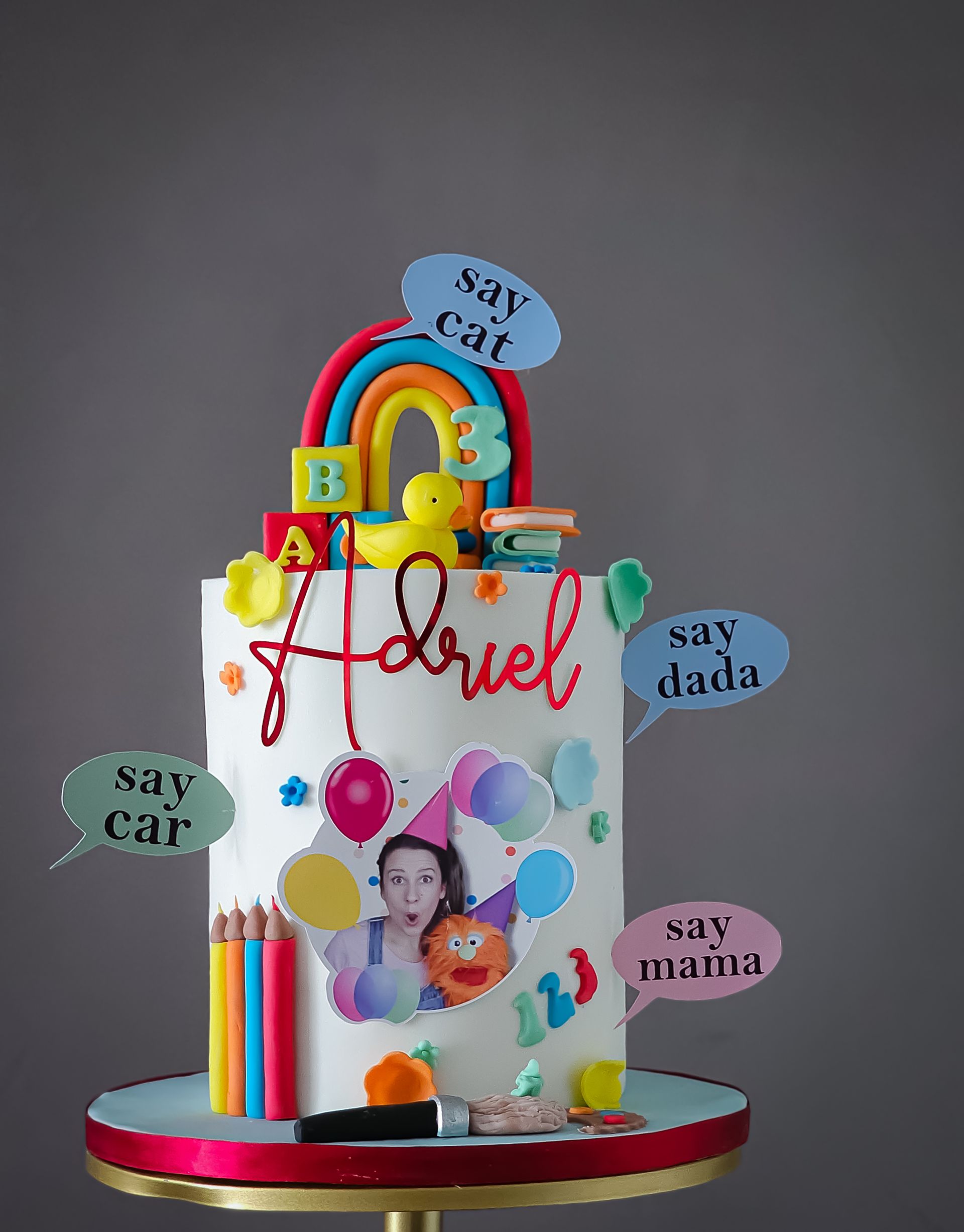 Cake with Adriel's name, a rainbow, and toy-themed decorations. Balloons, pencils