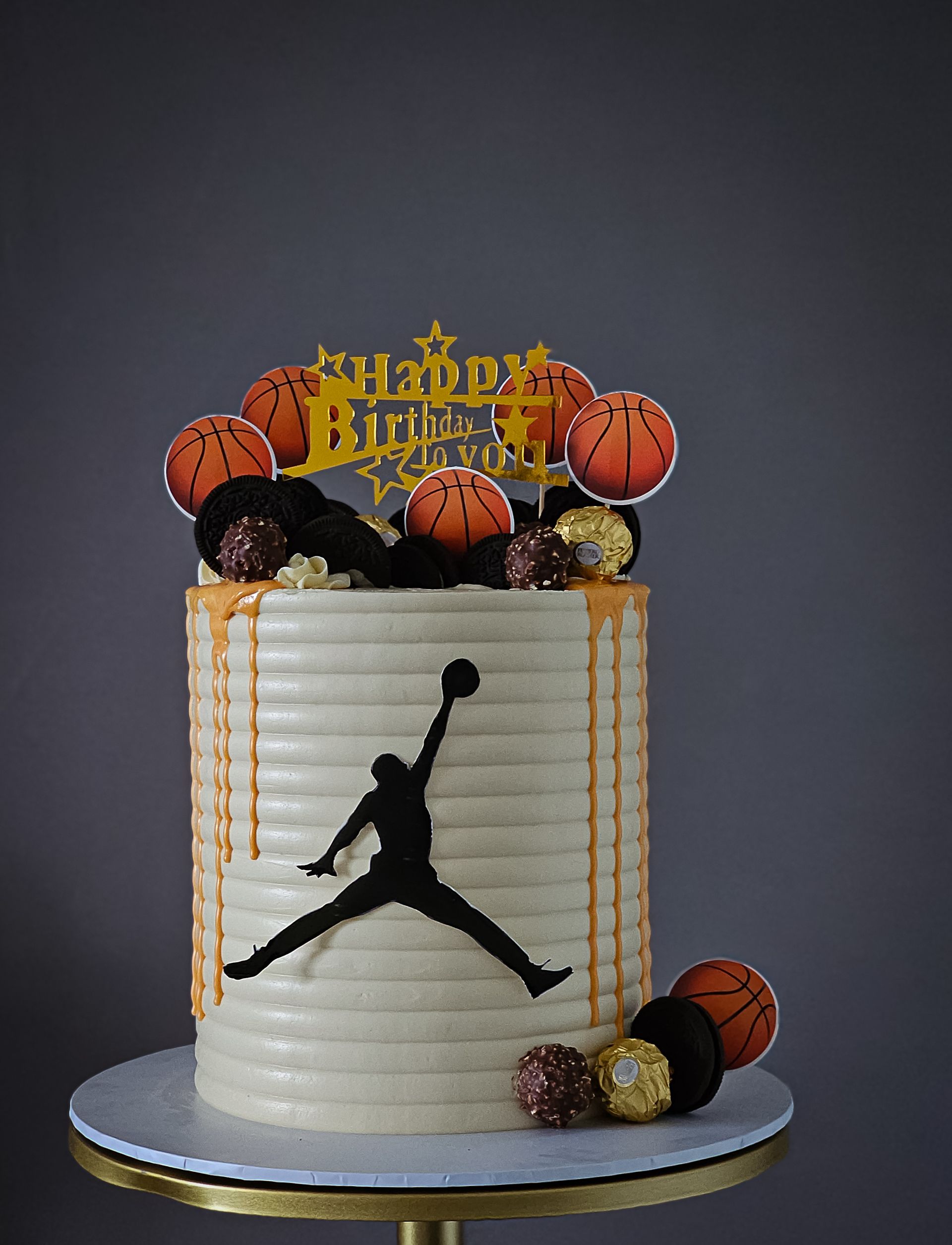 Cake decorated with basketballs, a silhouette of a basketball player, gold dripping, and
