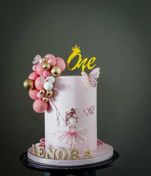 Pink and gold birthday cake with a ballerina design, balloons, and a 