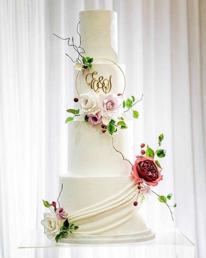 Elegant white tiered wedding cake with floral decorations and initials.