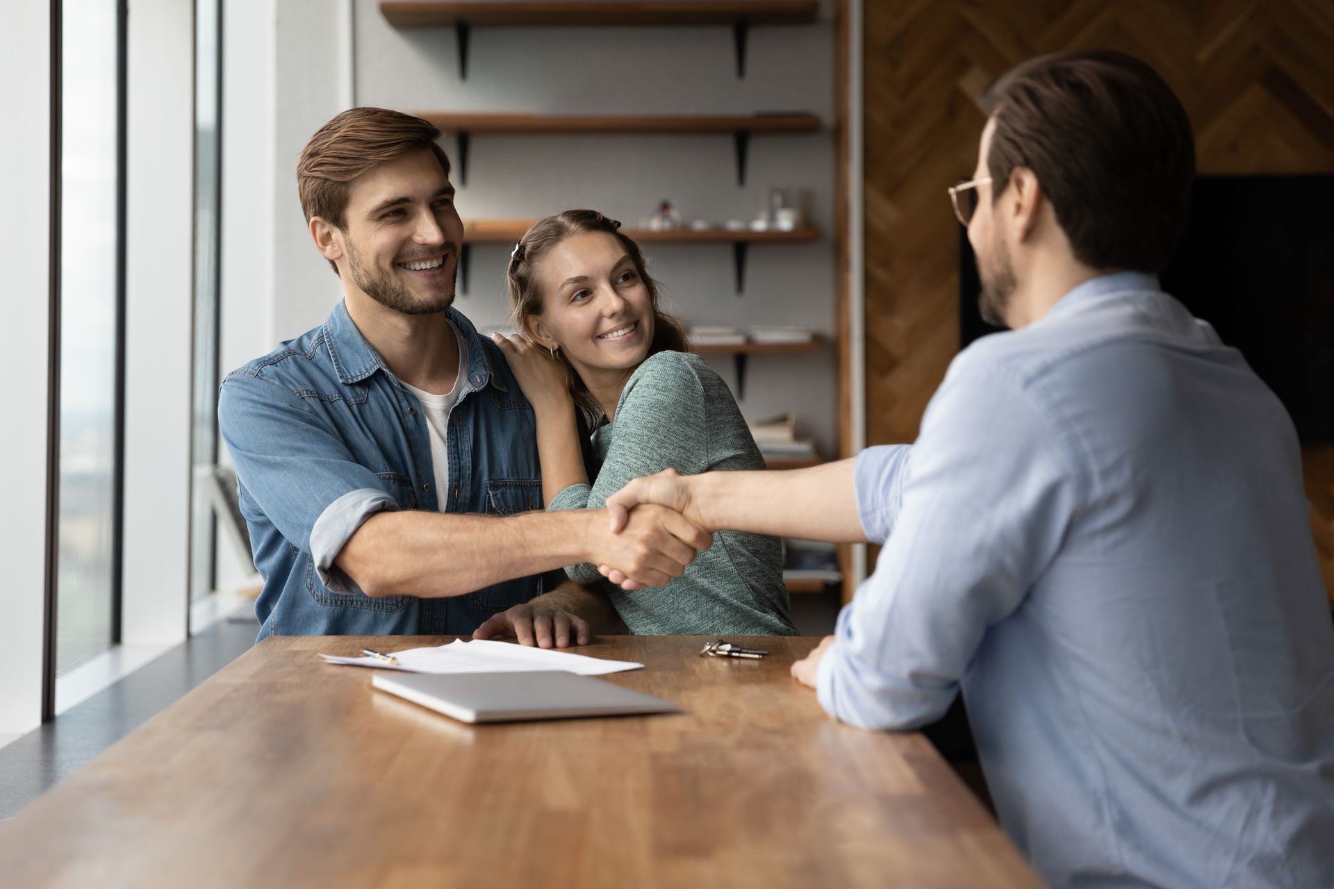 A man and woman are shaking hands with a real estate agent while sitting at a table.