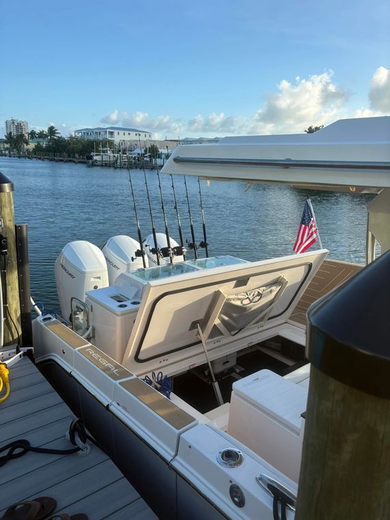 Fishing boat cockpit on calm water at sunset, with rods, outboard motors, and an American flag