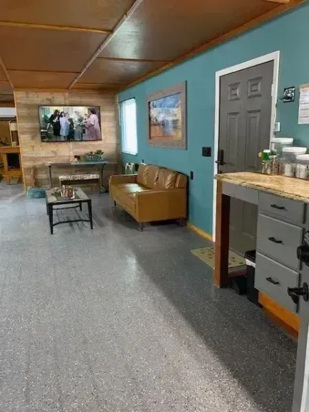 Living room with tan couch, wall-mounted TV, blue walls, and a small kitchen counter on the right