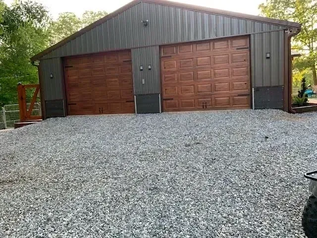 Gravel driveway leading to a brown metal garage with three doors and trees in the background