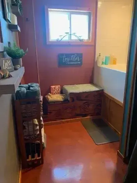 Small restroom with orange floor, wood trim, sink, window, and a wicker storage bench.