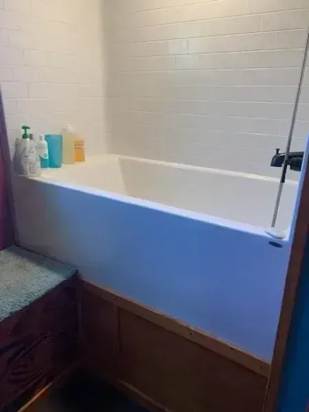 Bathroom with a white tub, blue paneling, and bath products on the ledge near a shower curtain.