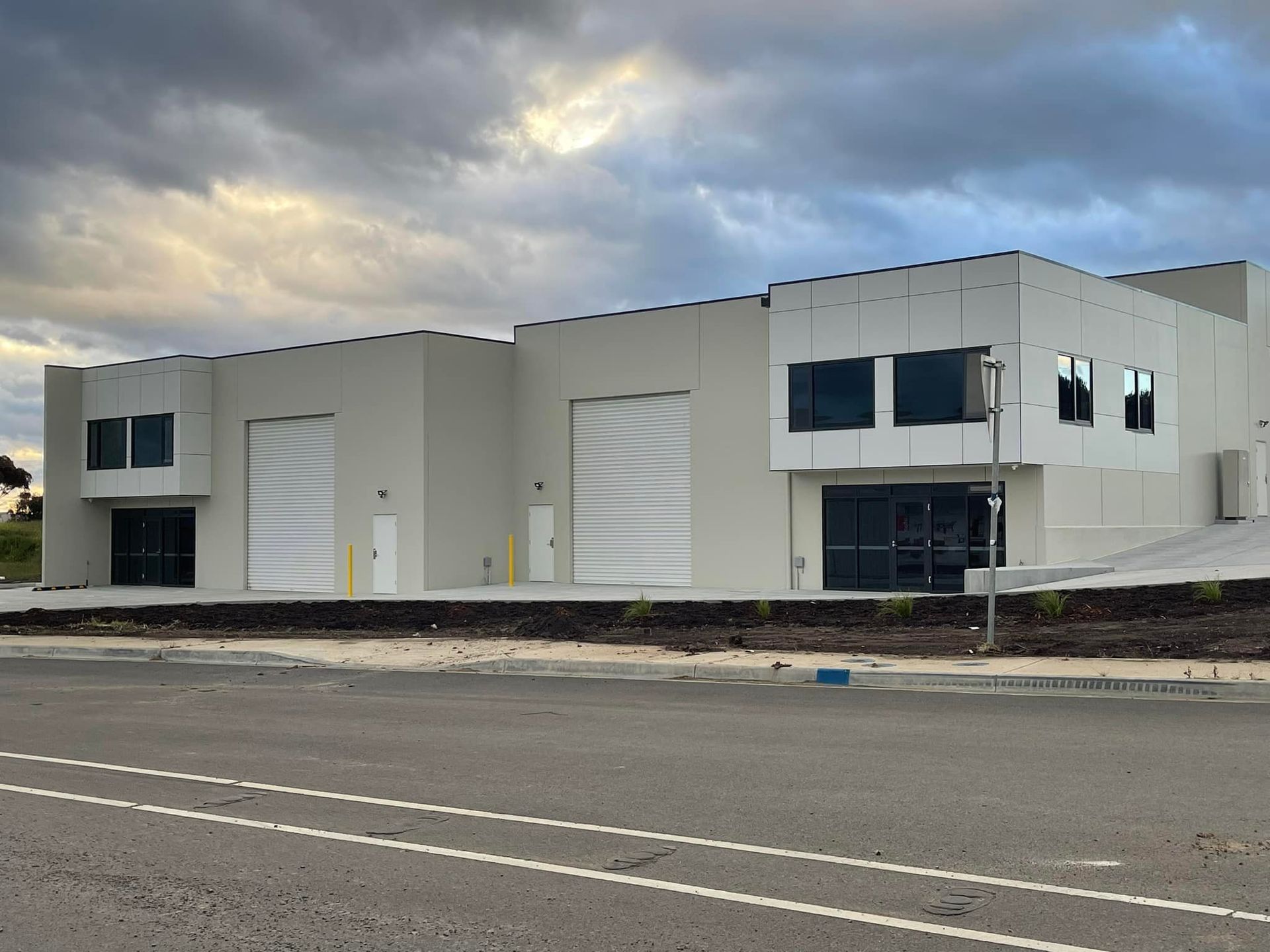 A large white building with a lot of windows is sitting next to a road.