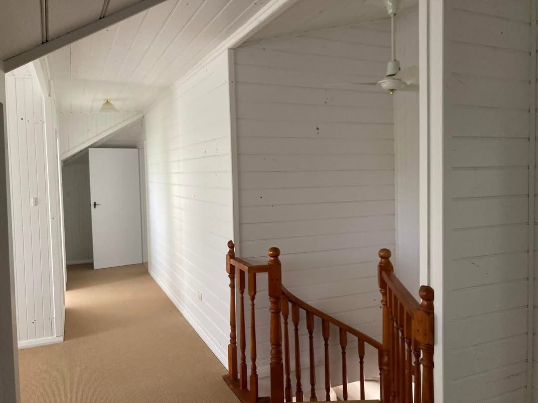 Hallway with wooden staircase, white walls, and beige carpet.