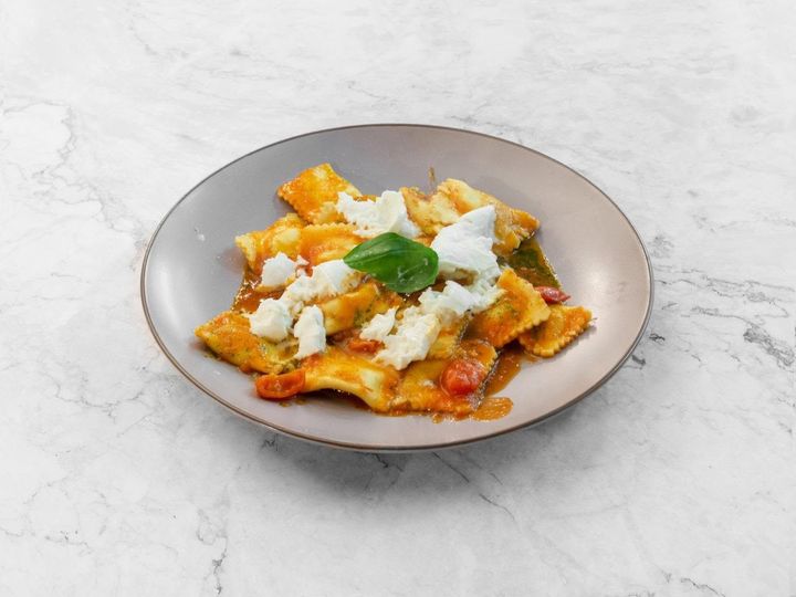 Piatto di pasta con salsa di pomodoro, basilico e formaggio fuso su una superficie di marmo chiaro.