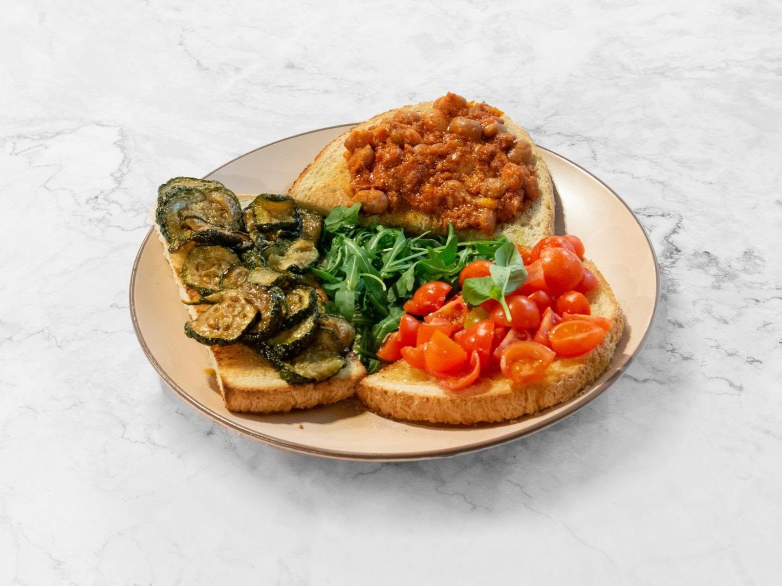 Piatto di bruschette con funghi saltati, pomodori, verdure e un condimento saporito su un tavolo bianco.