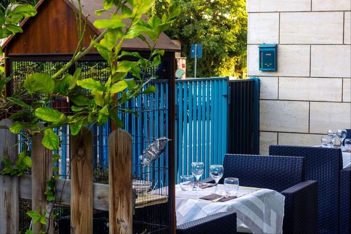 Cancello blu da patio accanto a un tavolo apparecchiato all'aperto, con vegetazione e un muro di pietra sullo sfondo.